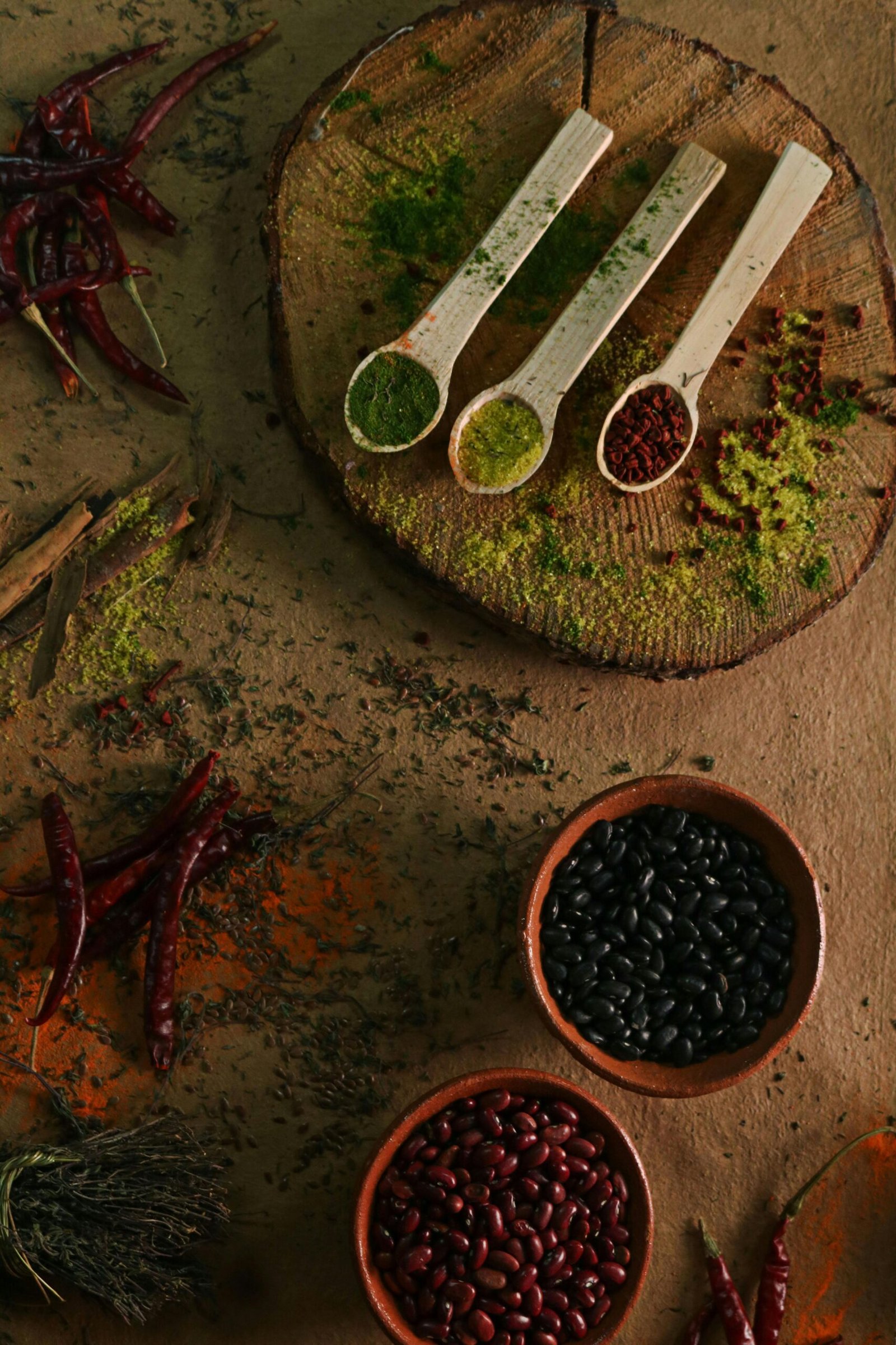 A top-down view of various spices and beans arranged on a rustic wooden surface for culinary art.
